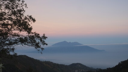 Aerial view of yellow sunrise over white puffy clouds with mountains on horizon. View on mountains and yellowy sky above clouds.
