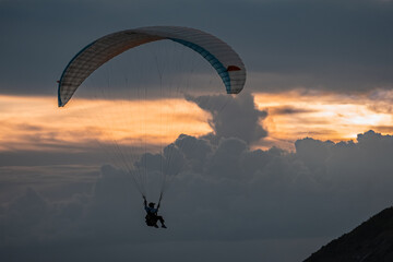 Paragliding in Phuket during sunset. People enjoy parasailing at beach during sunset time