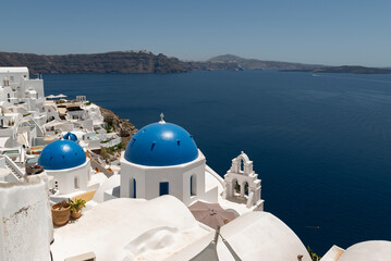 View of iconic blue domes and white buildings in Santorini with a stunning backdrop of the Aegean Sea.