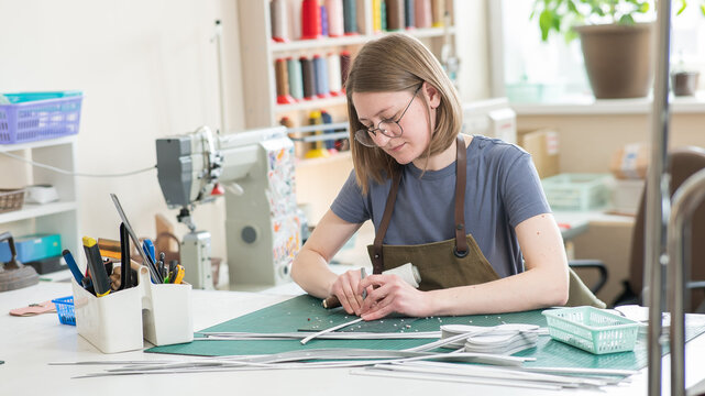 A woman makes holes in a leather belt in a workshop. - Powered by Adobe