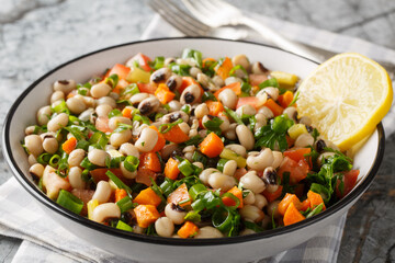 Winter salad with black-eyed beans, carrots, onions, tomatoes, basil, parsley dressed with olive oil closeup on the plate on the table. Horizontal