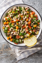 Fasolia mavromatika or black-eyed pea salad with carrot, leek, tomato and herbs closeup on the plate on the table. Vertical top view from above