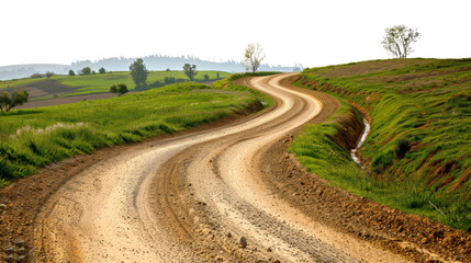 Naklejka premium Winding dirt road through green countryside, bordered by fields and trees, leading into hills under a clear sky.
