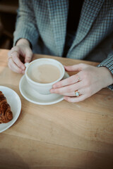 Hands holding a cup of coffee next to a croissant.