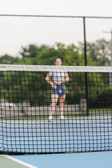 Blurred young woman behind pickleball net on outdoor court