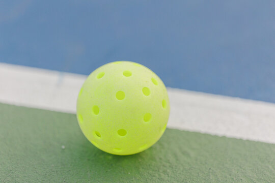Neon green pickleball on green court with white line, close-up.