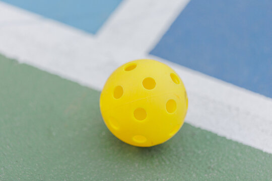 Yellow pickleball resting on green court near white line, close-up.