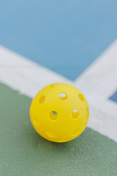 Yellow pickleball on court edge, close-up view showing its texture.