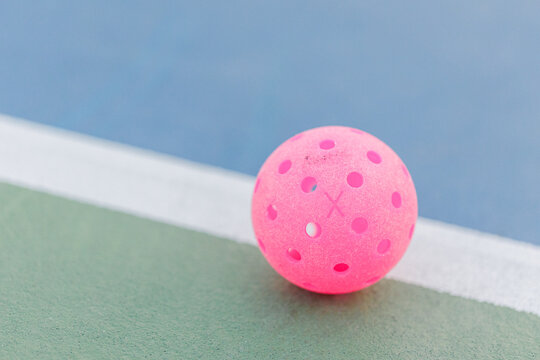 Close-up of a pink pickleball on a court line.