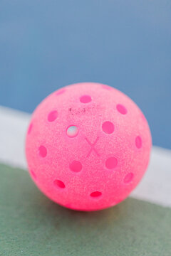 Close-up of a pink pickleball on a court.