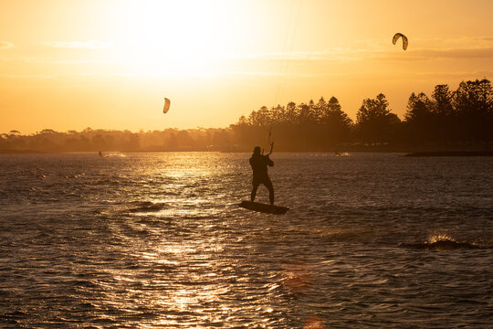 Kite surfer silhouetted at sunset getting flight on the water