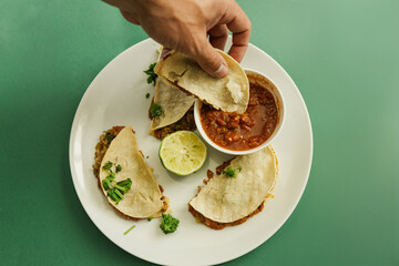 Hand holding taco over plate with salsa and lime on green background
