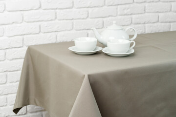 Beige Tablecloth on White Brick Wall With Teacups and Teapot