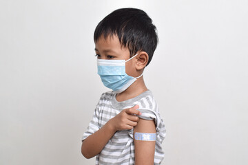 Asian boy using face mask with plaster bandage on his arm after vaccination. Vaccine injection. Child immunization. Health services for children. copy space