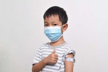 Asian boy wearing face mask giving thumbs up and showing his arm with bandage after getting vaccination. Child immunization. Protect children with vaccine concept. copy space