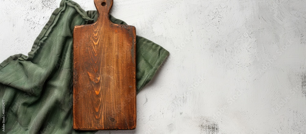 Poster A vintage rectangular cutting board with a handle is placed on a white table beside a green towel, accompanied by a blank area on the left for text or design in a copy space image.