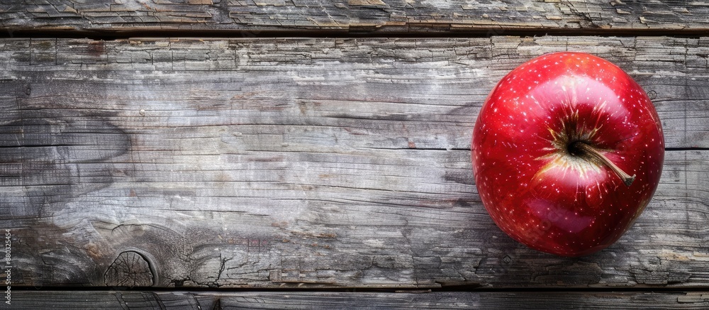 Poster A vibrant red apple resting on a rustic brown frame atop a gray wooden surface in a top-down view with copy space image included.
