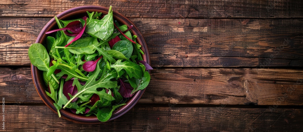 Poster a bowl of fresh green salad featuring spinach, arugula, and beetroot leaves on a rustic wooden surfa