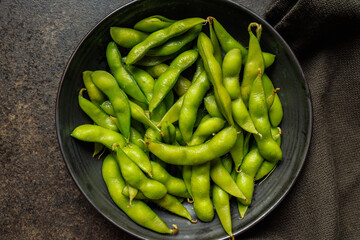 Green edamame pods. Fresh soybeans on plate on black table. Top view.