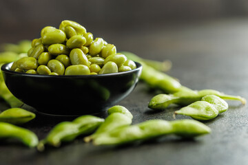 Green edamame pods. Fresh soybeans in bowl on black table.