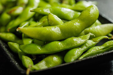 Green edamame pods. Fresh soybeans on plate on black table.