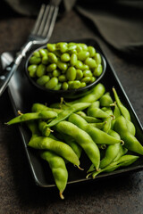 Green edamame pods. Fresh soybeans in bowl on black table.