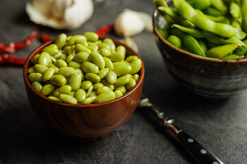 Green edamame pods. Fresh soybeans in bowl on black table.
