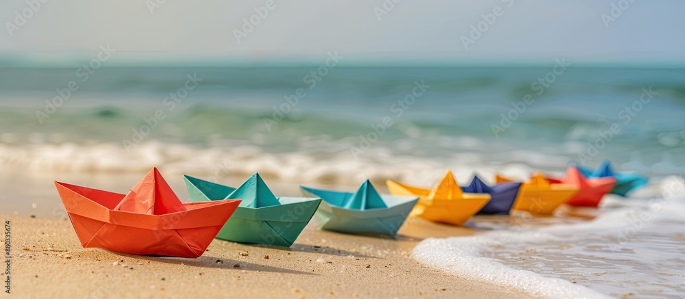 Poster paper boats of various colors arranged on the sandy beach near the sea with copy space image