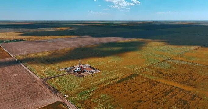 Flying closer to the little location in the dessert for drilling the natural resources. Clouds throw shadows on the immense field on sunny day.