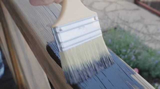Brush painting wooden railings of an open veranda with oil-based impregnation in rosewood color