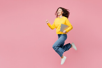 Full body side view young IT woman wear yellow sweatshirt casual clothes jump high hold use work on...