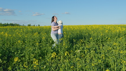 Fototapeta premium Small Boy Enjoy Playing With His Mom In A Yellow Flowering Rapeseed Field. Farmland With Yellow Flowering Rapeseed. Play On Field Outdoors.