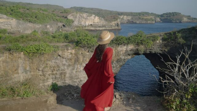 Nusa penida island, Bali, indonesia. 4K video Young woman red dress stand relaxing at viewpoint broken beach, beutiful broken beach,Nusa Penida island. Popular travel destination on Bali, indonesia.
