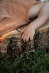 small toddler with blue eyes hold the stump at green nature field on sunset time