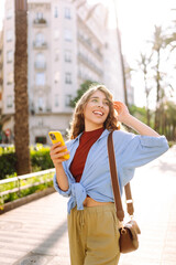 Woman traveler with a mobile phone on the street city. Young Woman texting, browsing, using her smartphone on a warm sunny day. Business, technology, blogging, communication concept.