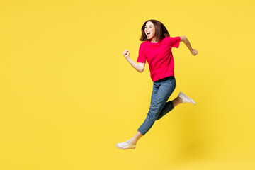 Full body side profile view excited happy young woman she wears pink t-shirt casual clothes jump high run fast hurry up isolated on plain yellow orange background studio portrait. Lifestyle concept.