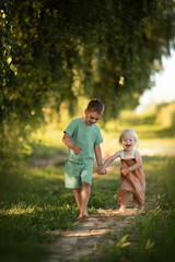 Fototapeta premium two small brothers run together at green nature field on sunset time