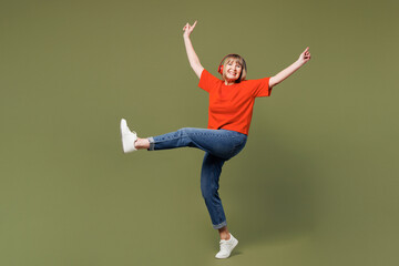 Full body elderly blonde woman 50s years old she wears orange t-shirt casual clothes listen to music in headphones raise up hands isolated on plain pastel green background studio. Lifestyle concept.