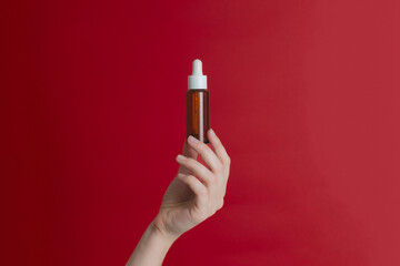 Serum glass unbranded bottle (essential oil) with pipette on red background. Natural moisturizing, nourishing cosmetics for skin, beauty and spa