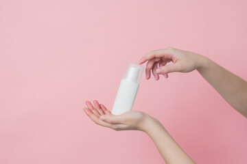 White unbranded cream bottle with pump in hand on pink background. Concept of beauty. Product cosmetic advertising