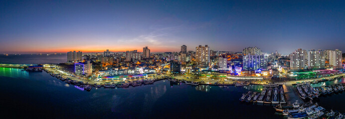 Bangeojin, Dong-gu, Ulsan, South Korea - January 11, 2024: Panoramic and sunset view of fishing boats moored on the sea at Bangeojin Port with buildings and apartments
