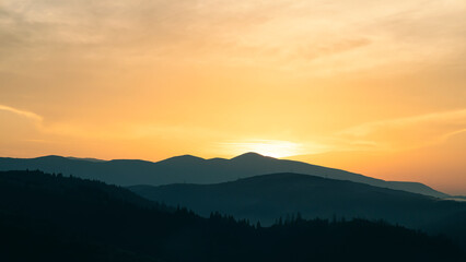 Sunset above horizon line with sun setting down behind mountains