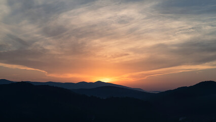 Sunset above horizon line with sun setting down behind mountains