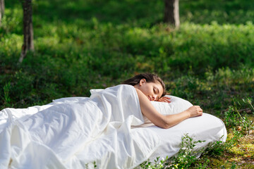 Woman sleeps on a mattress in the summer forest. The girl is resting in nature