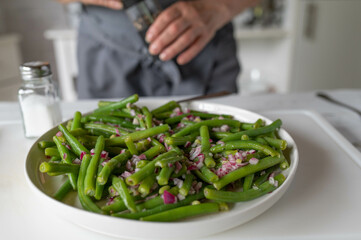 Green bean salad with red onions. Marinated with vinegar and oil. Served by a woman with apron in the kitchen
