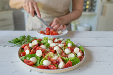 Woman preparing a fresh caprese salad with tomatoes and mozzarella cheese in the kitchen