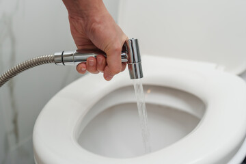 hand using chromium bidet shower spraying in toilet bowl