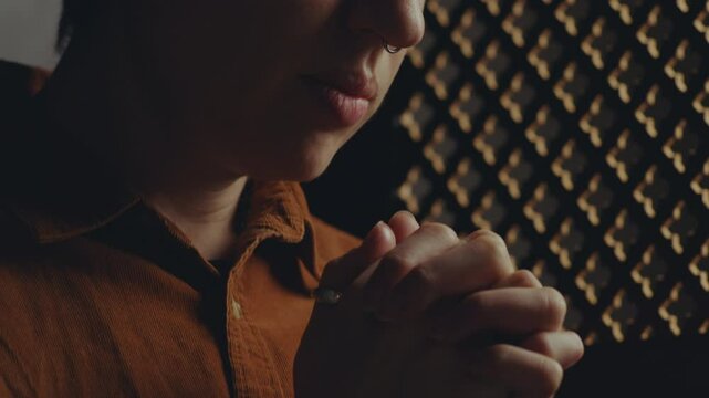 Young woman holding palms together and saying contrition prayer with eyes closed during confession in church. Close-up view