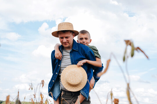 Agronomist, father and son together in agriculture field with soybeans. The man shows the boy ripe soy. Quality control of crops. Front view