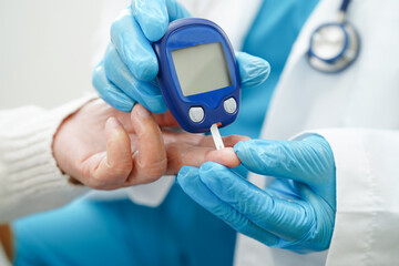 Asian doctor using digital glucose meter for check sample blood sugar level to treatment diabetes.